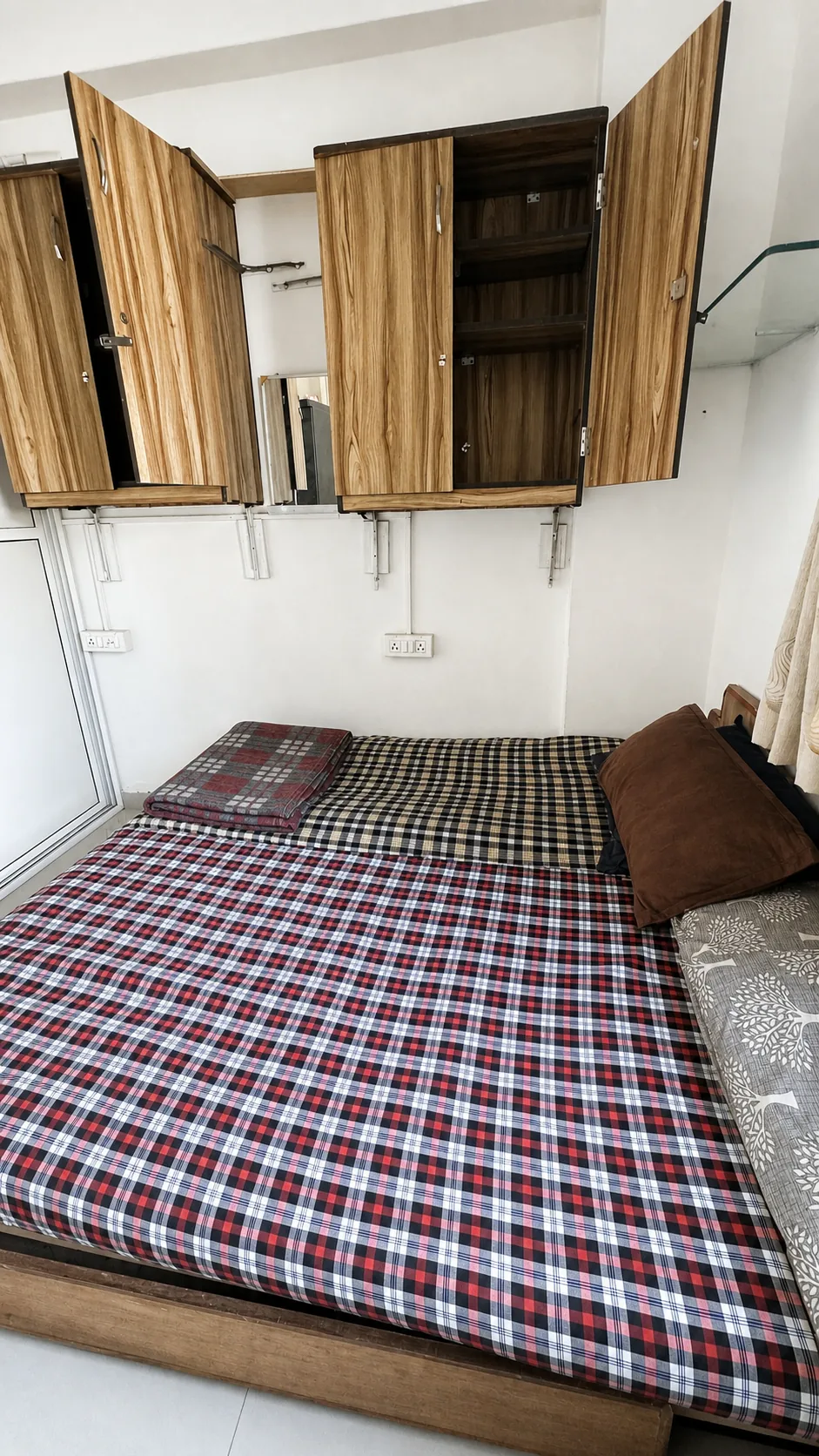 Shared room with checked bedding and wooden wall cabinets