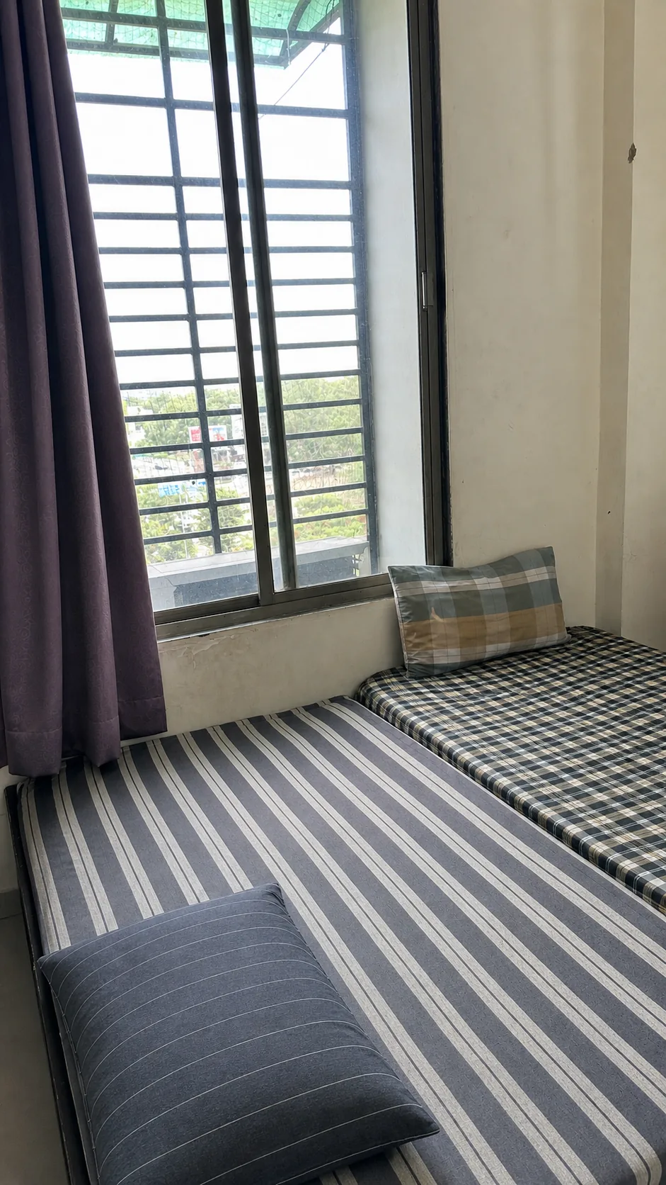Shared sleeping space beside a grilled window with purple curtains
