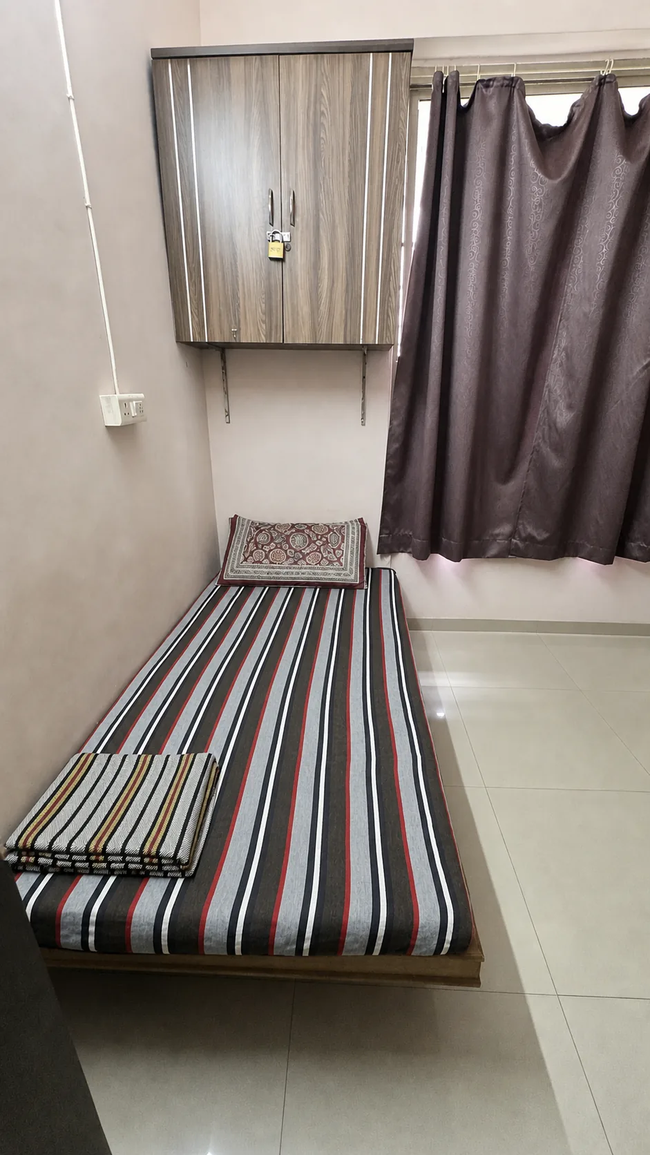 Single furnished bed below a wall-mounted wooden storage cabinet