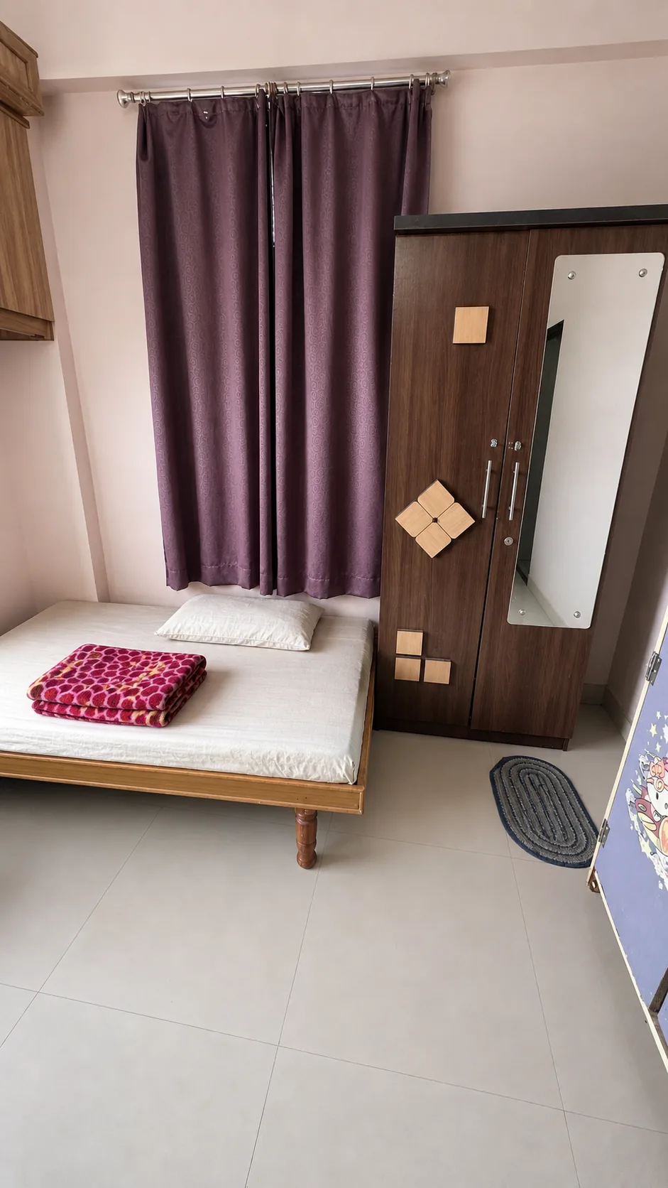 Furnished bed beside a wooden wardrobe with a full-length mirror